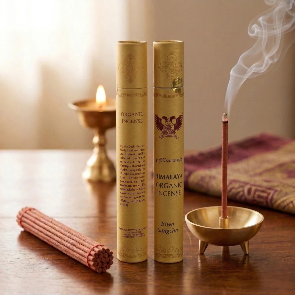 Himalayan organic incense Riwo Sangcho — two gold tubes with Garuda emblem, smoking brass holder, butter lamp