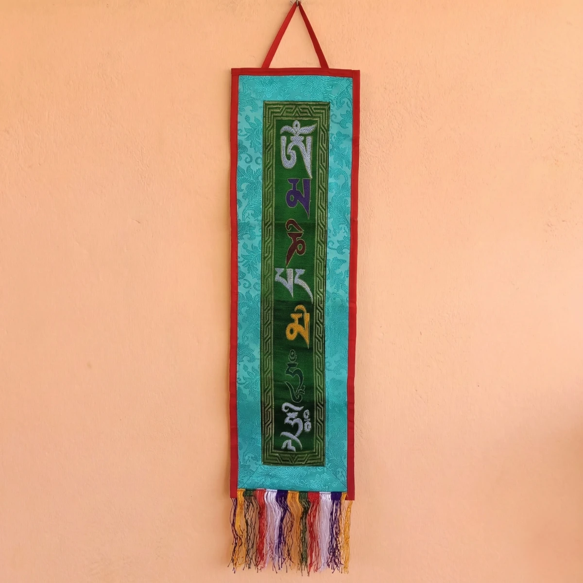 Om Mani Padme Hum Tibetan wall hanging — forest green panel, teal brocade border, multicolour fringe tassel