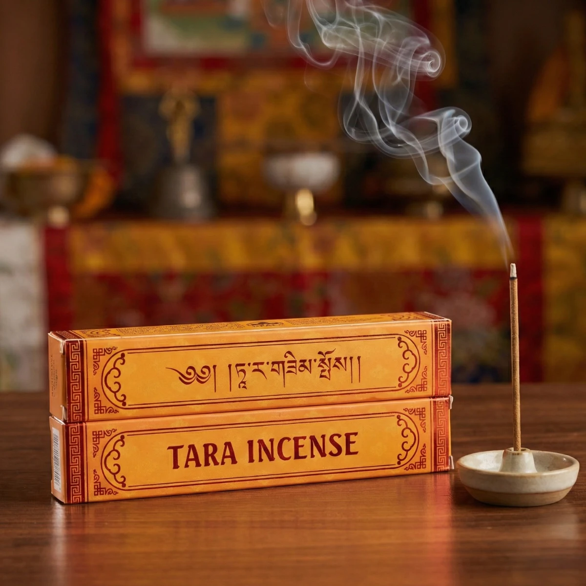 Tara Incense — two saffron boxes stacked on wood, lit stick in ceramic holder, Tibetan altar backdrop